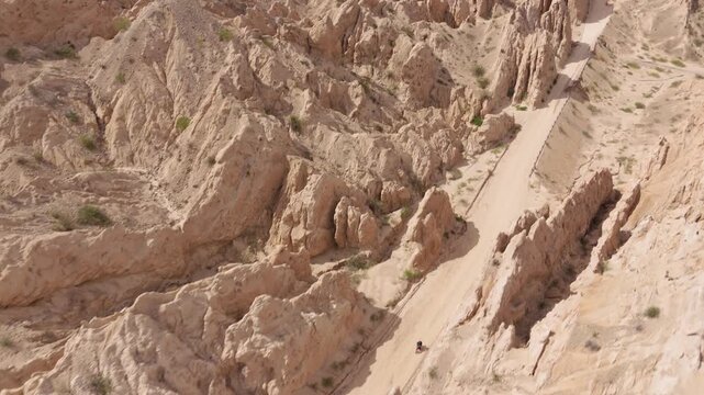 Motorbike passing towering sandstone formations in Quebrada de las Flechas, aerial ascend pullback at midday, Salta Region Argentina