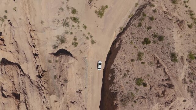 White car driving through Quebrada de las Flechas sandstone canyon, aerial top down tracking follow in desert
