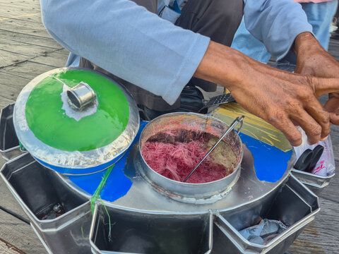 Indonesian street vendor's hands packing traditional pink cotton candy into a plastic bag. Ideal for editorial articles, culinary blogs, cultural documentary presentations, and travel website design
