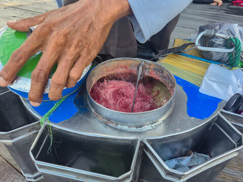 Indonesian street vendor's hands packing traditional pink cotton candy into a plastic bag. Ideal for editorial articles, culinary blogs, cultural documentary presentations, and travel website design
