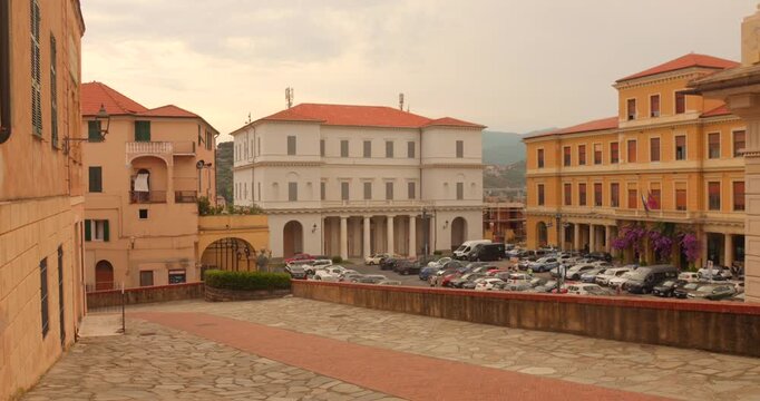 Historic main square in Imperia with classic buildings and parked cars, overcast sky