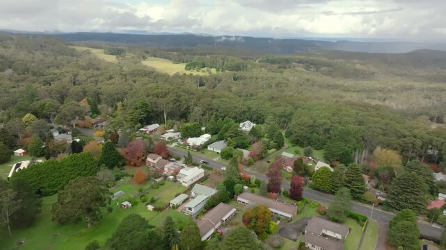 Drone aerial flying above Bundanoon with residential streets bordered by native eucalyptus forest in the Southern Highlands, New South Wales, Australia.
