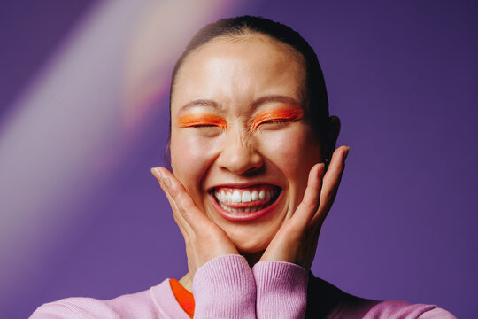 Asian woman with bold makeup smiling joyfully in a studio portrait