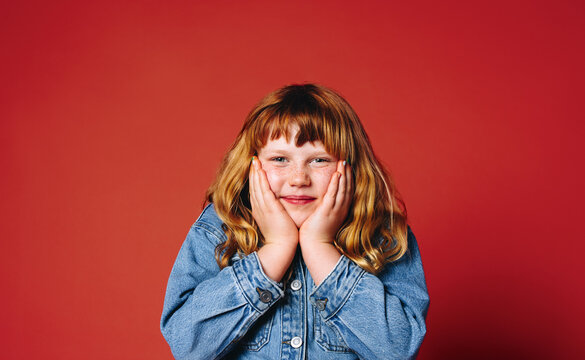 A young girl portrait in denim jacket posing with hands on face in studio