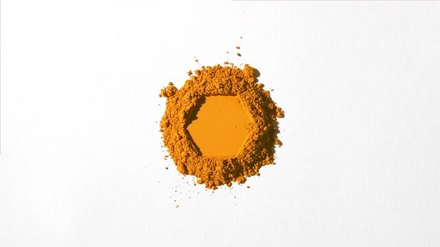 Top view perspective shot of a stack of orange powder with a hexagonal impression on a dim grey background illuminated by revolving directional light casting dynamic shadows