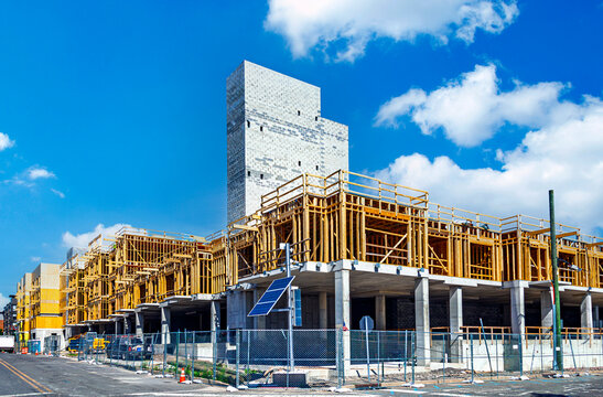 Large-scale residential construction site showing concrete pillars, a cinder block core, and extensive wood framing under a sunny blue sky.