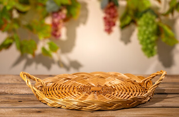 Obraz premium Wicker basket on wooden table with blurred grape leaves for rustic autumn harvest product scene