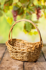 Obraz premium Empty wicker basket on rustic wooden table with blurred grape leaves for autumn harvest product mockup