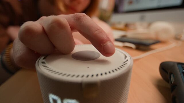 Hand of unrecognizable person pressing button on smart speaker, controlling smart home assistant. Ideal for smart home technology, IoT devices, and modern digital lifestyle advertising