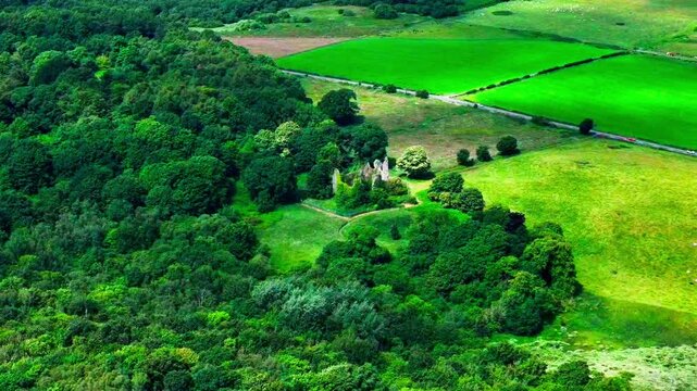 Cinematic aerial view, ancient stone ruins surrounded by mature woodland and open countryside, filmed at Old Auchans near Dundonald, Ayrshire, Scotland