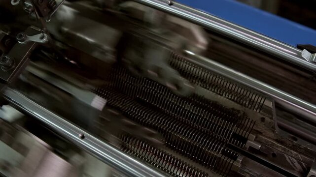 Macro view focuses on moving metal components inside knitting machine in slow motion. Automated textile equipment demonstrates accurate manufacturing process.