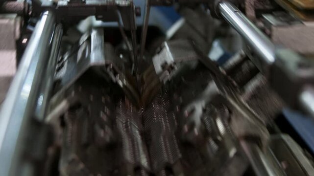 Close up captures moving knitting machine needles during textile manufacturing. Precision mechanism operates inside automated industrial equipment.