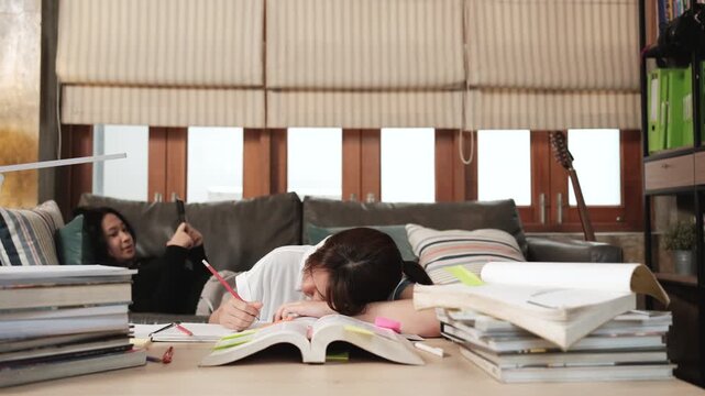 Two College Asian friends, teenage girl tired and burned out from overwhelmed homeschooling, study pile of books, stressed learning at home, her friend wakes up while napping, education exam support.
