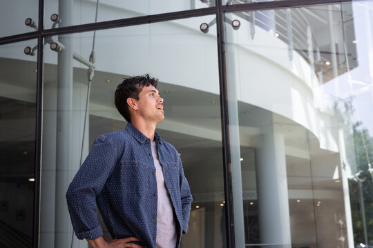 Confident man looking up near modern glass building