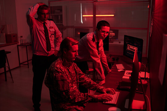 Diverse security officers and military soldier working on computer during cyber attack emergency in dark control room. Image suitable for cybersecurity and national defense marketing