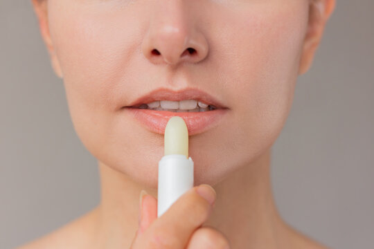 Close up of young woman face applying hygienic white moisturizing lip balm to her lips.