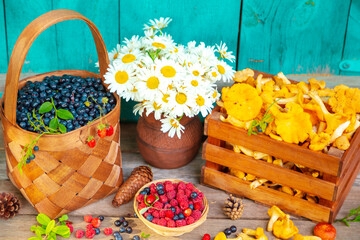 Ripe juicy blueberries in a wicker basket, raspberries, chanterelles in a wooden crate, and chamomile flowers. © lizavetta