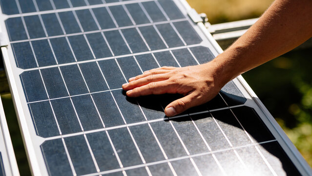 Closeup view of hand touching solar panel in agrivoltaics system with crops below