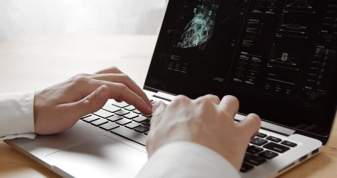 Person works on a laptop displaying a rotating digital visualization of a human heart with medical data.