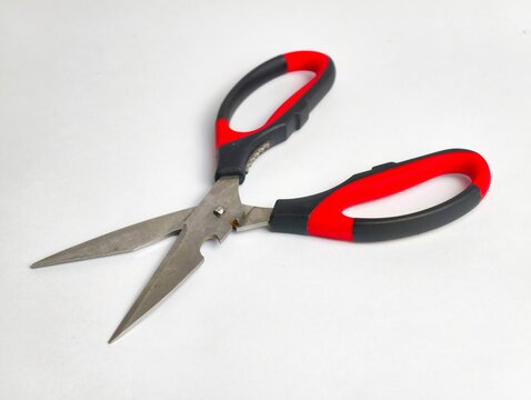 Open multi-purpose kitchen scissors with stainless steel blades, red and black ergonomic handles, and notch functions, isolated on a white surface.