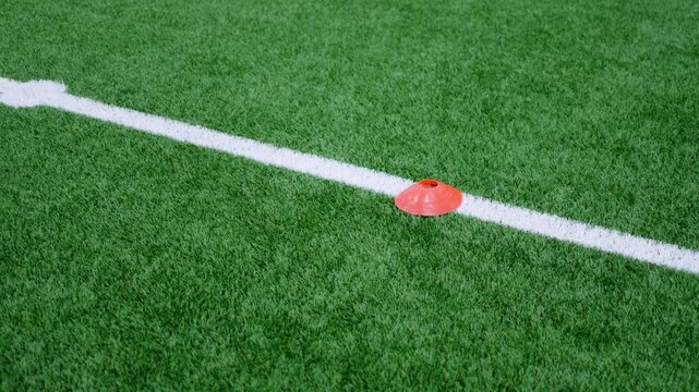 Training cone sits on marking line of artificial grass pitch. Sports field layout provides clear guidance during active tactical exercises