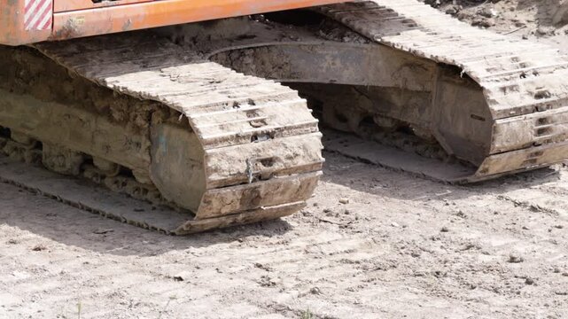 Weathered metal tracks and embedded soil reveal relentless work on unfinished ground. The gritty texture and mechanical mass convey raw power meeting rugged terrain