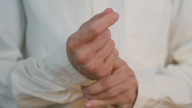 Close up man hands carefully fastens button on white shirt cuff. Elegant and precise gesture of businessman getting dressed, ready for formal event or meeting. Man in white shirt buttoning sleeve cuff