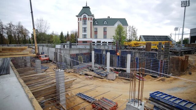 Bright truck crane stands near steel formwork shuttering panels. Construction area contains piles of timber dirt roads scattered tools