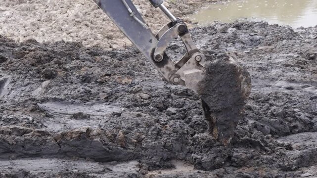 Raw industrial power meets stubborn, saturated soil; thick mud clings to the bucket as the machine wrestles the unyielding terrain