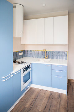 Modern kitchen interior featuring blue cabinetry, white countertops, and stainless steel appliances with wooden flooring and tiled backsplash in a contemporary design