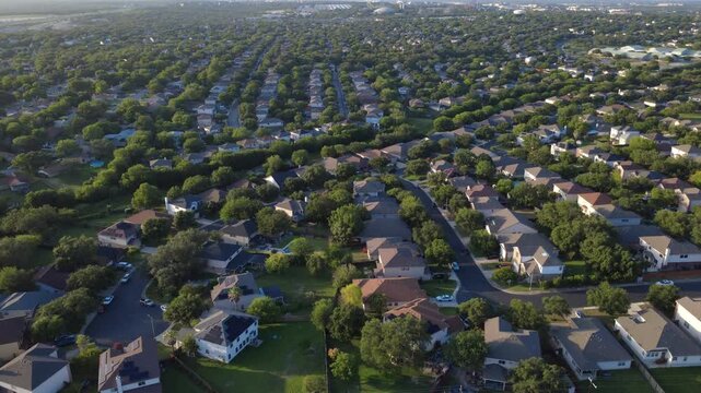 Looking straight down reveals curving asphalt streets, concrete driveways, solar paneled roofs in Spring Vistas subdivision. Private swimming pools dot shaded backyards. San Antonio, Texas