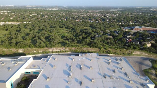 Direct top down viewpoint details flat commercial roofing panels, ventilation units, cooling systems bordering lush green woodlands near Culebra Road in Spring Vistas subdivision. San Antonio, TX