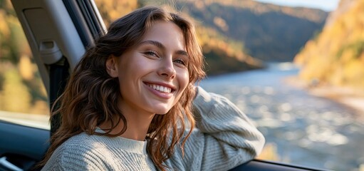 Obraz premium A woman enjoys the scenic autumn landscape with colorful hills and a shining river from inside a car.