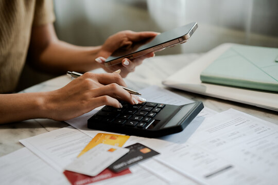 The close-up image shows a woman calculating various expenses with a calculator, credit cards, and documents, revealing debt, financial stress, money problems, and economic hardship.