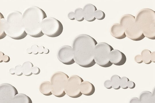 Flat lay pattern of small sculpted clay clouds in white and soft beige colors arranged on a plain light cream background, with shadows