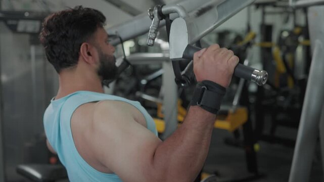 An Indian Asian fit young man using a lat pulldown machine, performing a resistance weight training exercise or workout targeting the back and shoulders in a modern gym. Fitness, bodybuilding concept