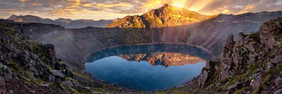 Majestic mountain lake reflects golden sunrise in a dramatic panoramic landscape.