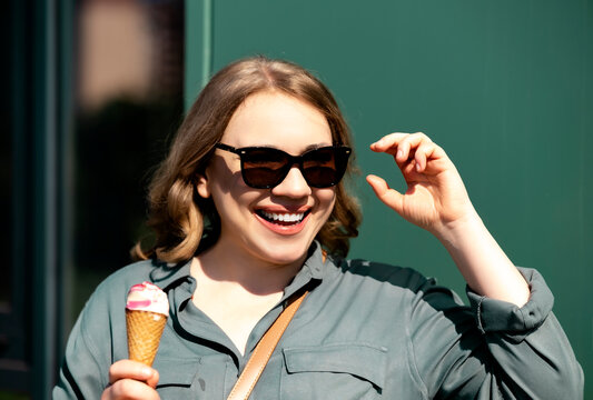 Cheerful smiling woman in sunglasses eating ice cream outdoors. Summer enjoyment and sweet dessert treat on sunny day.