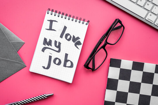 Find dream job. Handwritten motto I love my job in notebook on office desk on pink background top view