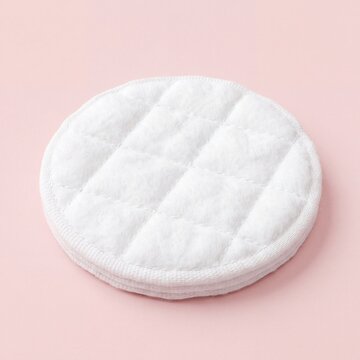 A single white quilted cotton facial cleansing pad isolated on a soft pastel pink background.