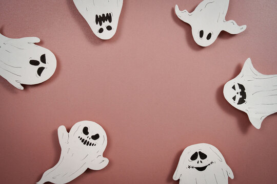Halloween craft background with white paper ghosts on pink surface with copy space