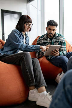 Two young professionals collaborate on a digital project while seated comfortably on beanbag chairs in a modern office setting