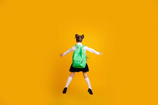 Excited schoolgirl jumping with green backpack on vibrant yellow background &mdash; back to school joy and playful childhood energy