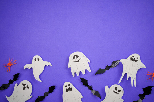 Halloween paper ghost and bat cutouts on purple background with copy space