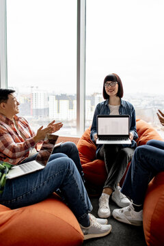 A diverse group of colleagues collaborates on laptops while seated on beanbag chairs near a large window