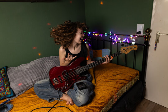 Teenage girl plays electric bass on bed in her bedroom