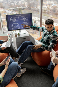 A team collaborates on automotive design concepts, reviewing blueprints on a large monitor while using laptops and tablets