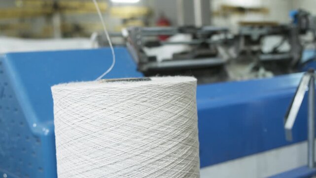 Close view shows yarn feeding advanced knitting machine inside modern textile factory. Automated production relies on steady thread supply for precise operation.
