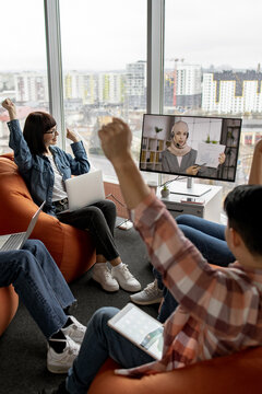 A group of young people are enthusiastically participating in an online lecture, raising their hands in a modern, casual learning environment