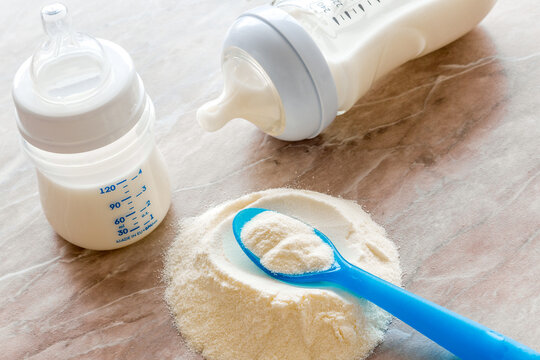 Baby food. Powder in spoon near baby bottle on brown background
